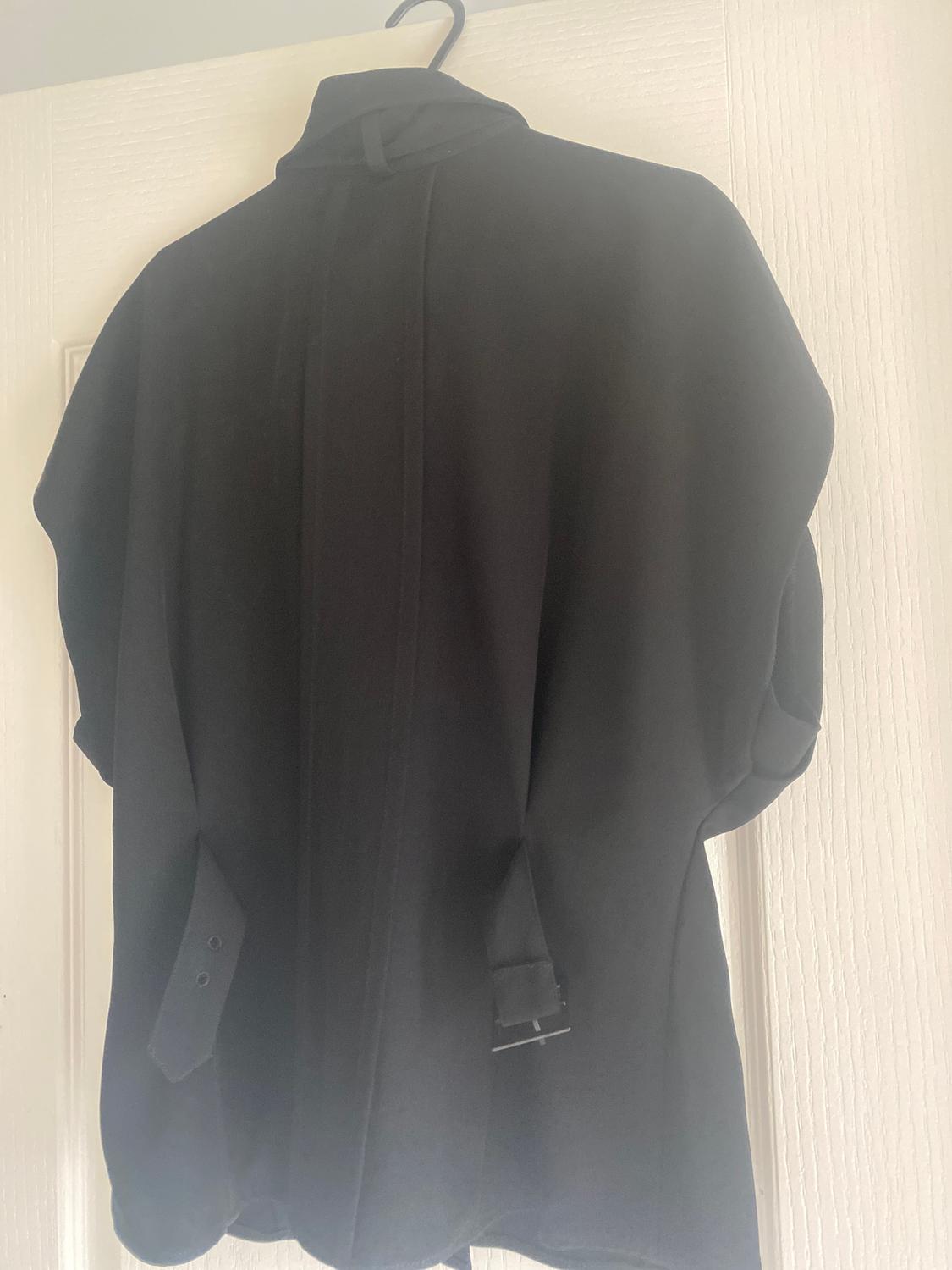 Black coat hanging on a hanger over a white door. The fabric is plain and has strap details on the back.