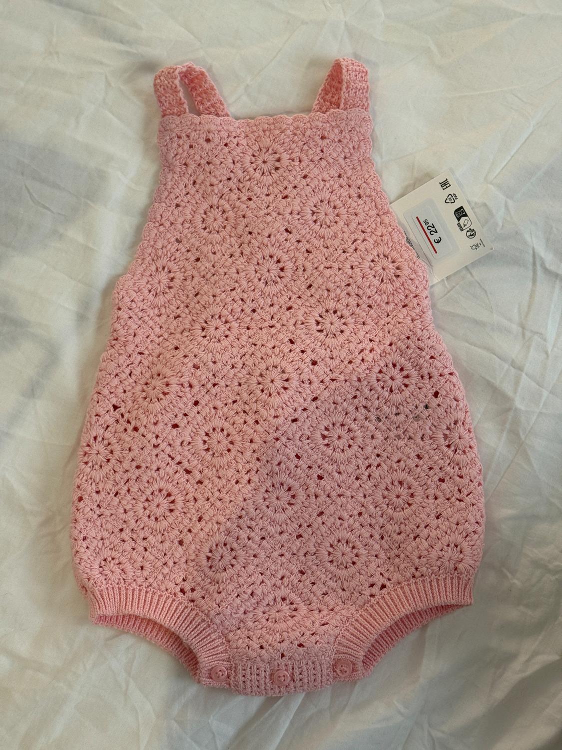 Pink crochet romper with straps and a floral design on white fabric. Visible tag with price of €22.99.