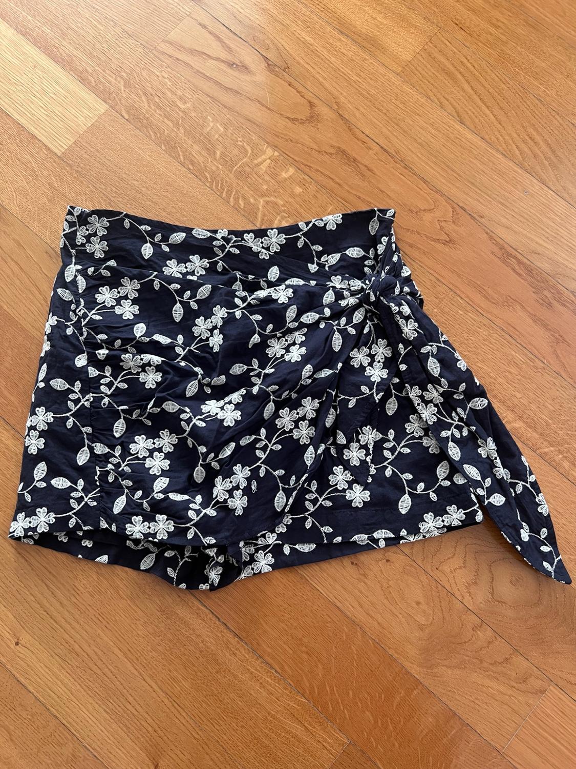 Dark-coloured culottes with white floral motifs and a side-knot detail, on a wooden floor.