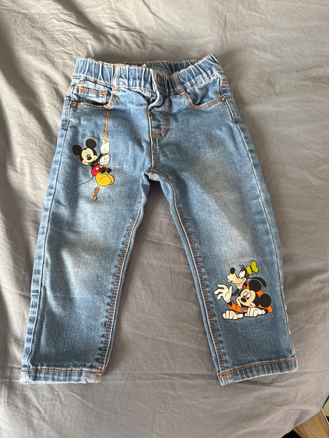 Children's jeans with cartoon character designs on the legs, on a grey surface.