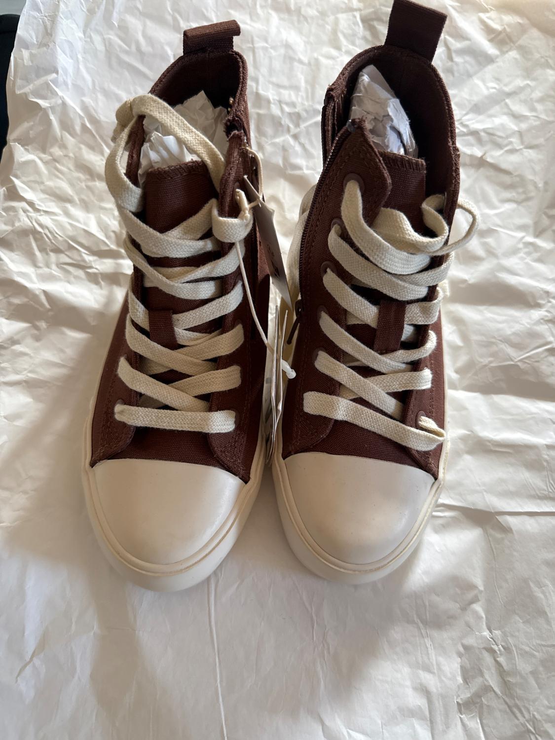 Brown high-top trainers with white laces on white crumpled paper. Casual and modern design.