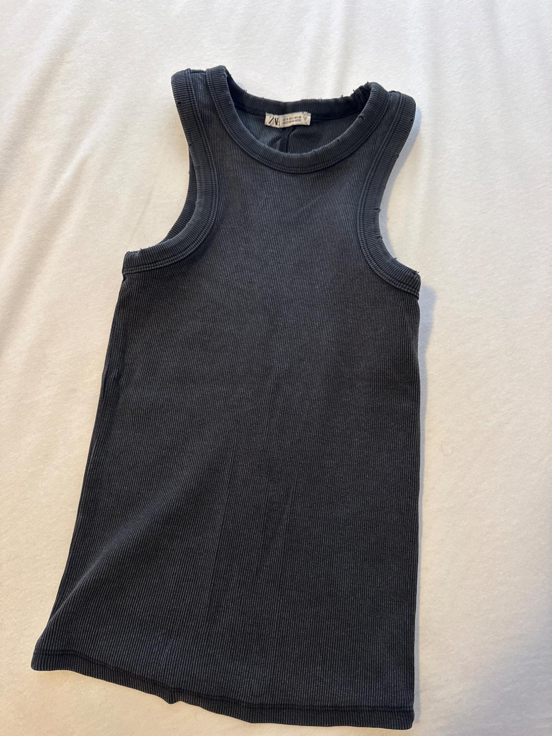 Dark grey ribbed vest top laid out on a white fabric. The neck label reads ZARA.