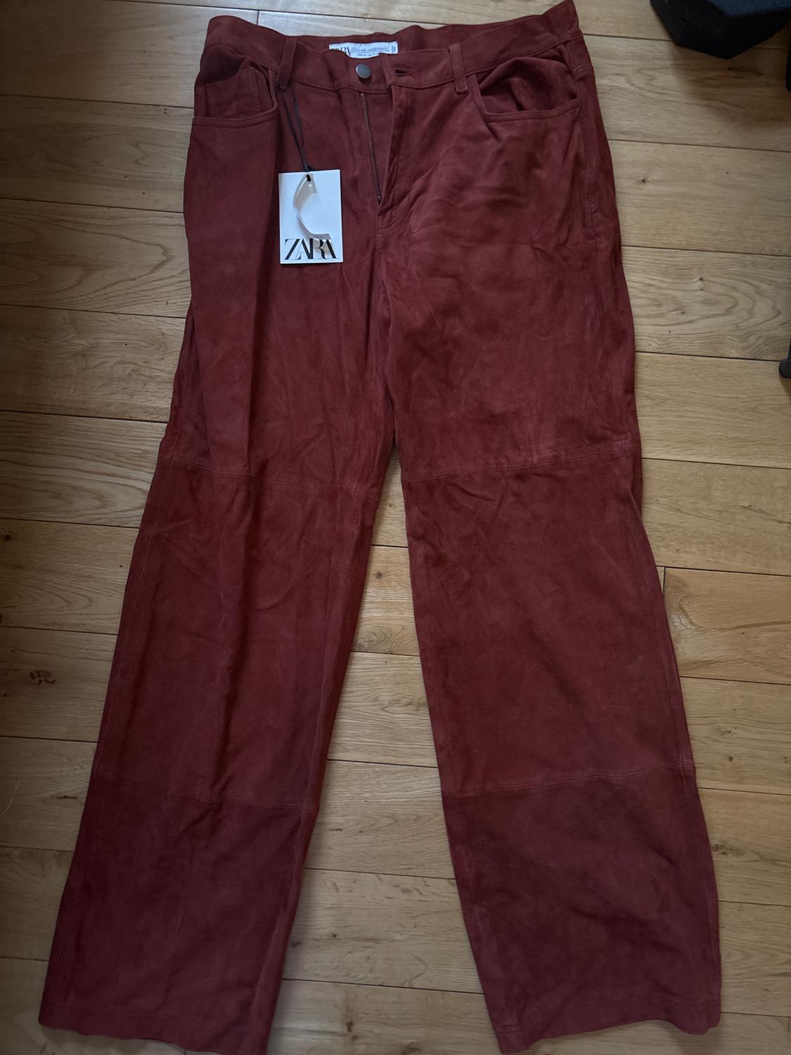 Russet-coloured wide-leg trousers on a light wooden floor. Visible label with the text "ZARA".