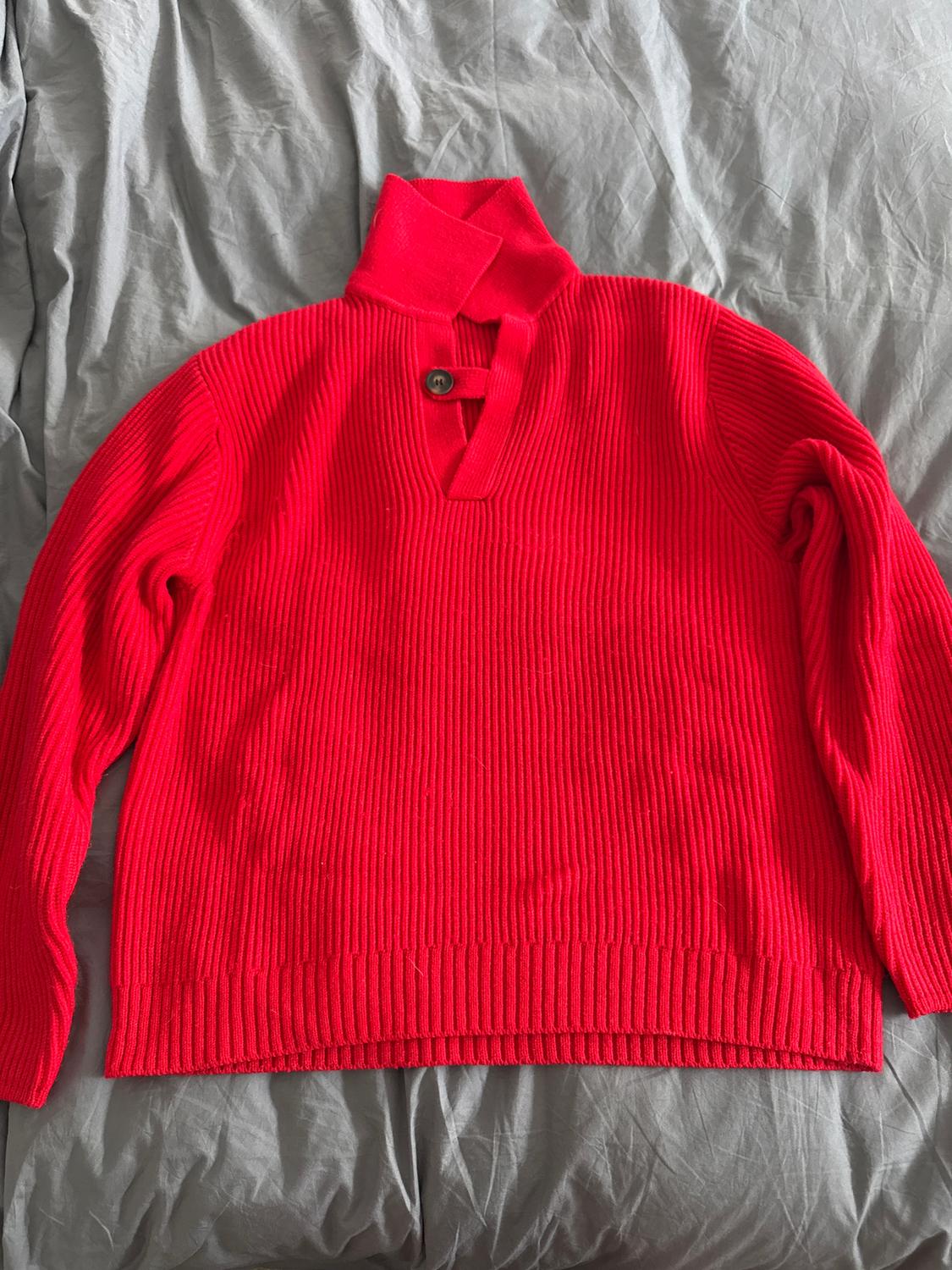 Chunky red knitted jumper with a high neck and one button, on a wrinkled grey surface.