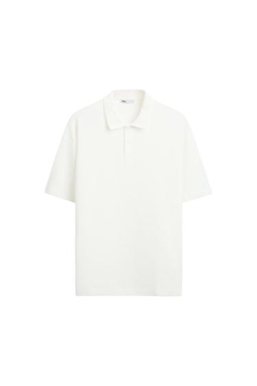 White textured short-sleeved polo shirt with a collar and buttons. Label with ZARA text on a white background.