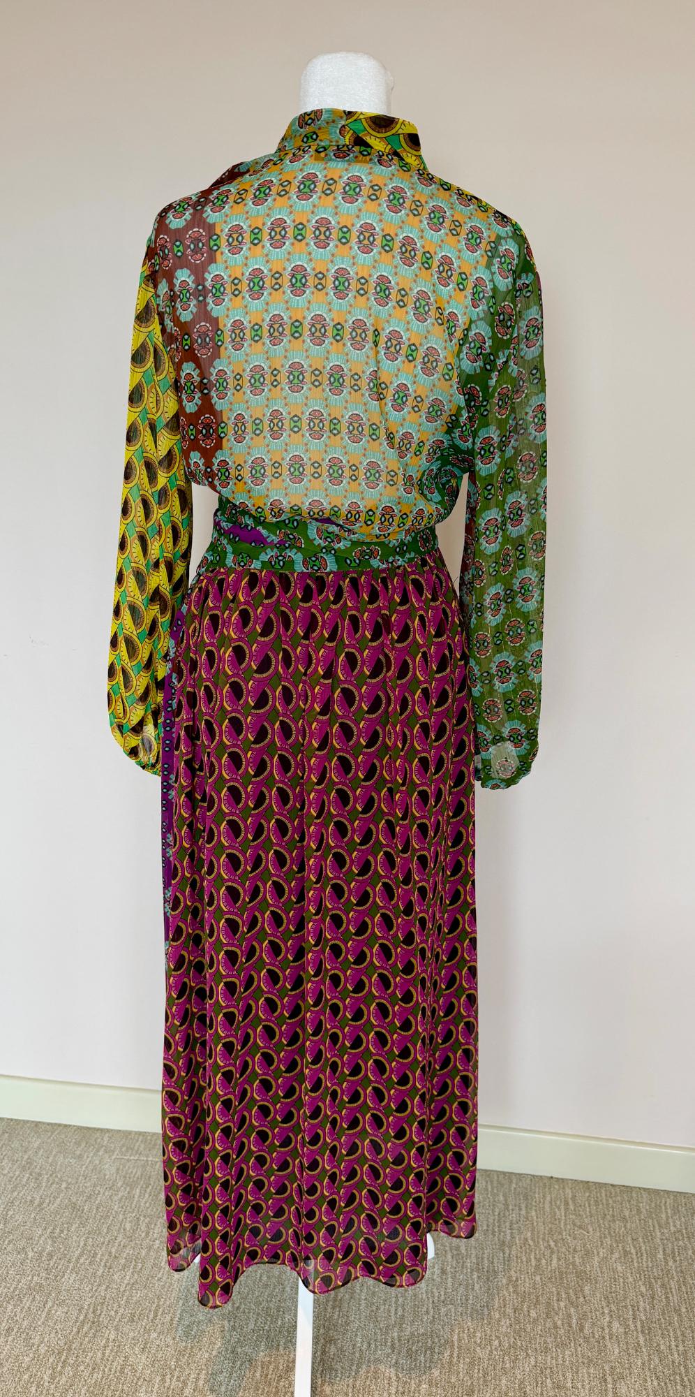 Mannequin with geometric print dress in green, yellow, and purple tones. White background and beige carpeted floor.