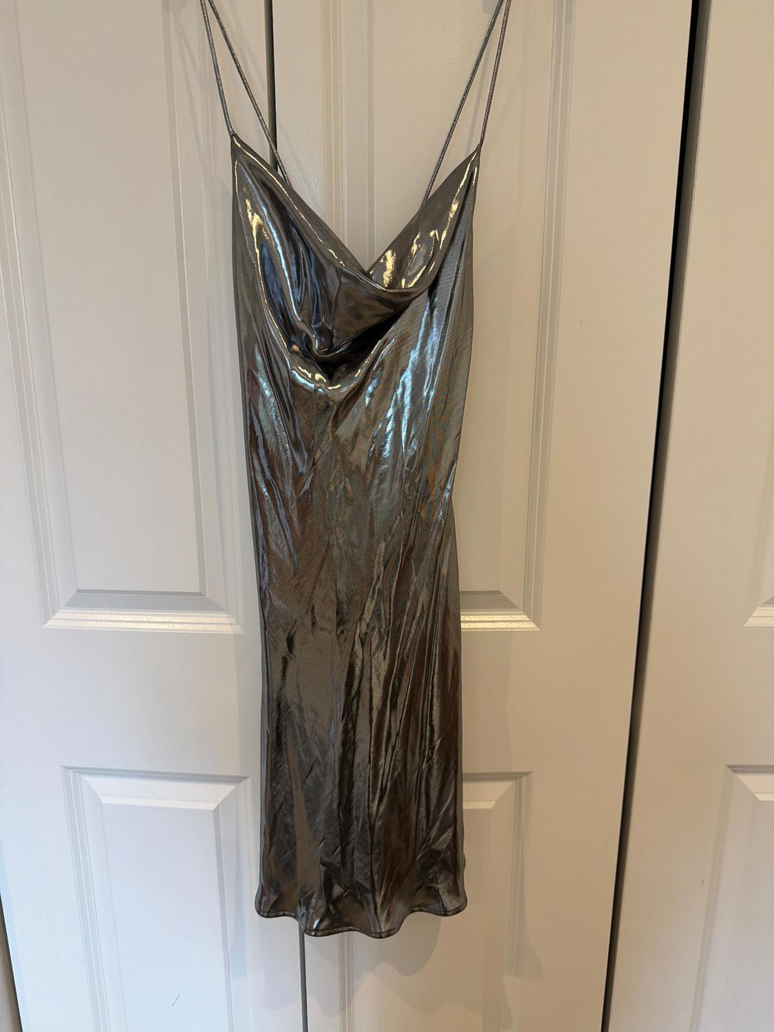 Silver metallic dress with spaghetti straps and a draped neckline, hanging on a white paneled door in a relaxed setting.
