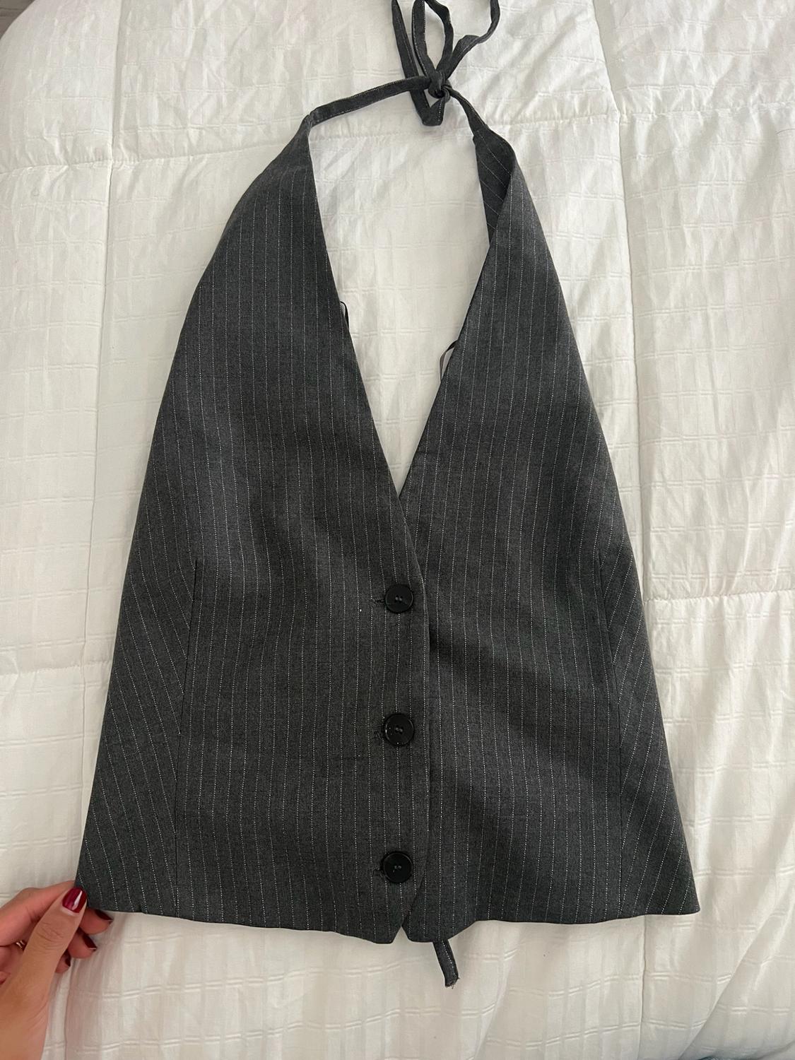 A gray pinstriped halter top with three buttons on the front rests on a white blanket. A hand with red-painted nails holds the edge.