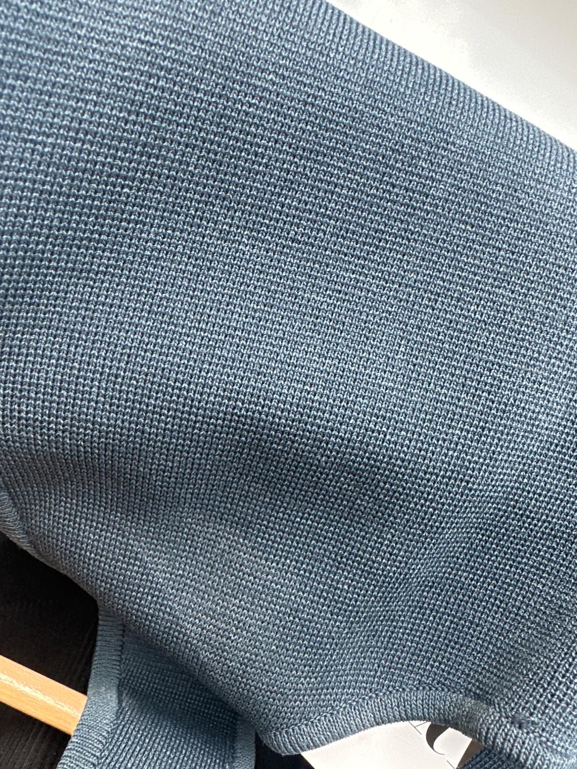 Close-up of a blue knit garment on a wooden hanger. The texture of the fabric is clearly visible.