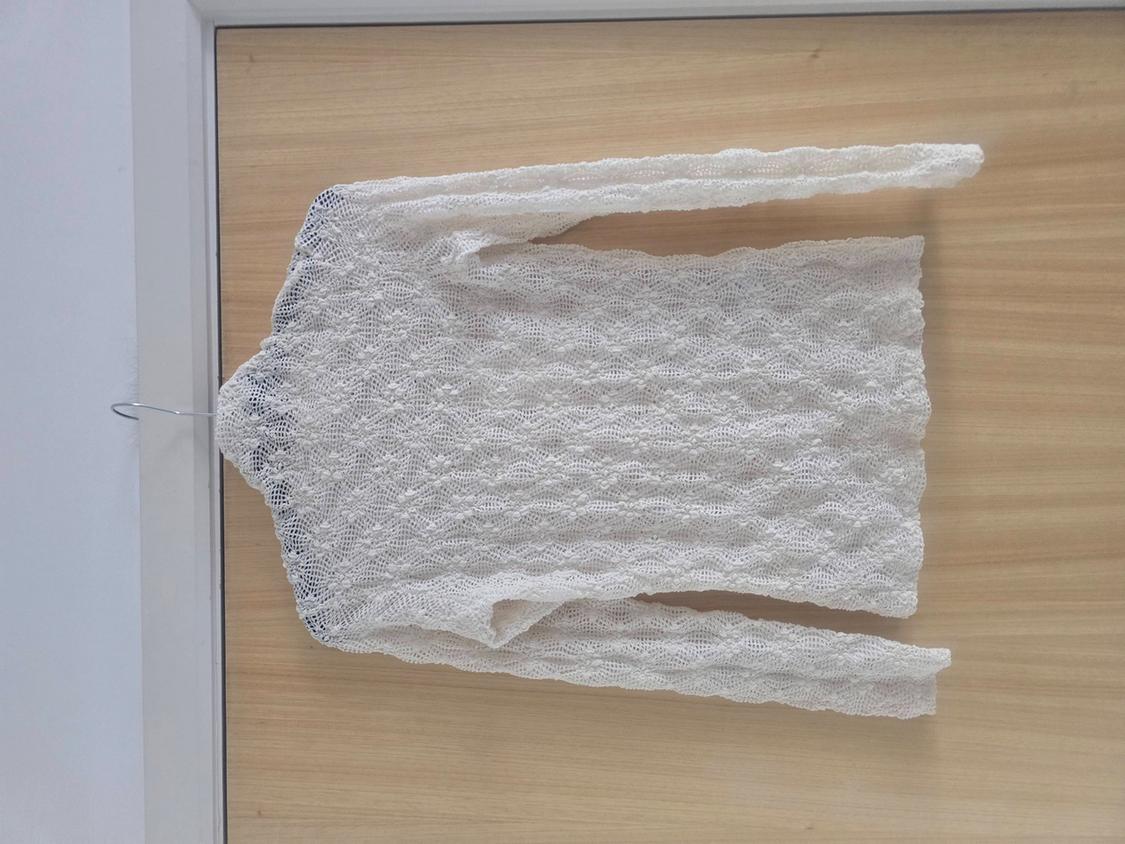 White lace jumper hanging on a hanger over a light wooden door.