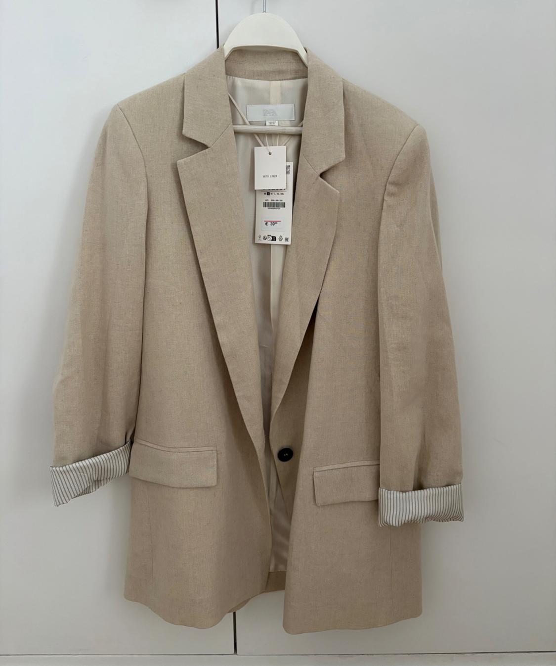 Beige blazer with pockets, hanging on a white background. Rolled-up sleeves with a striped lining. Labels with text ZARA, WITH LINEN, € 39.