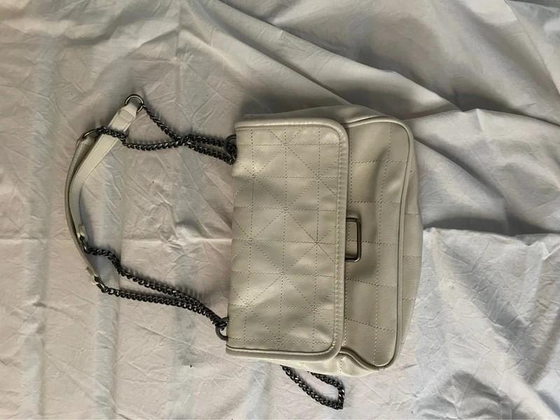 White bag with a quilted design and metallic chain on crinkled fabric.
