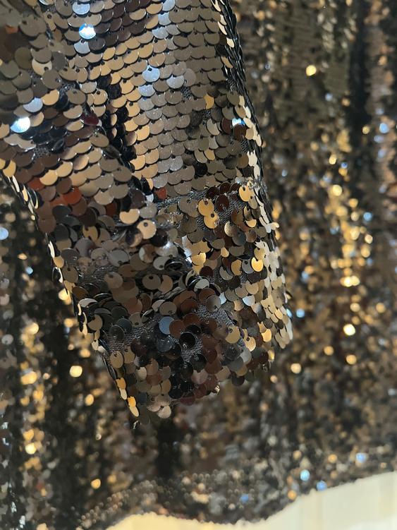 Shiny fabric with gold and silver sequins in the foreground, creating a luminous and festive effect.