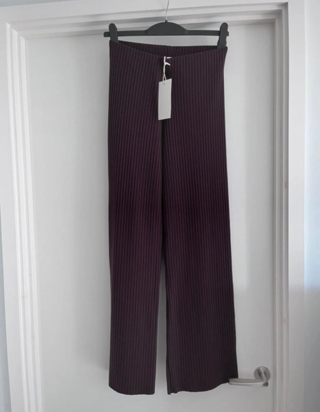 Dark, vertical striped trousers hanging on a black hanger over a white door. Label visible.