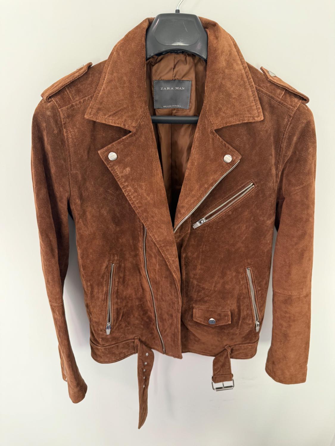 Brown suede biker jacket with zippers and a belt, hanging on a hanger against a white background. Text: ZARA MAN.