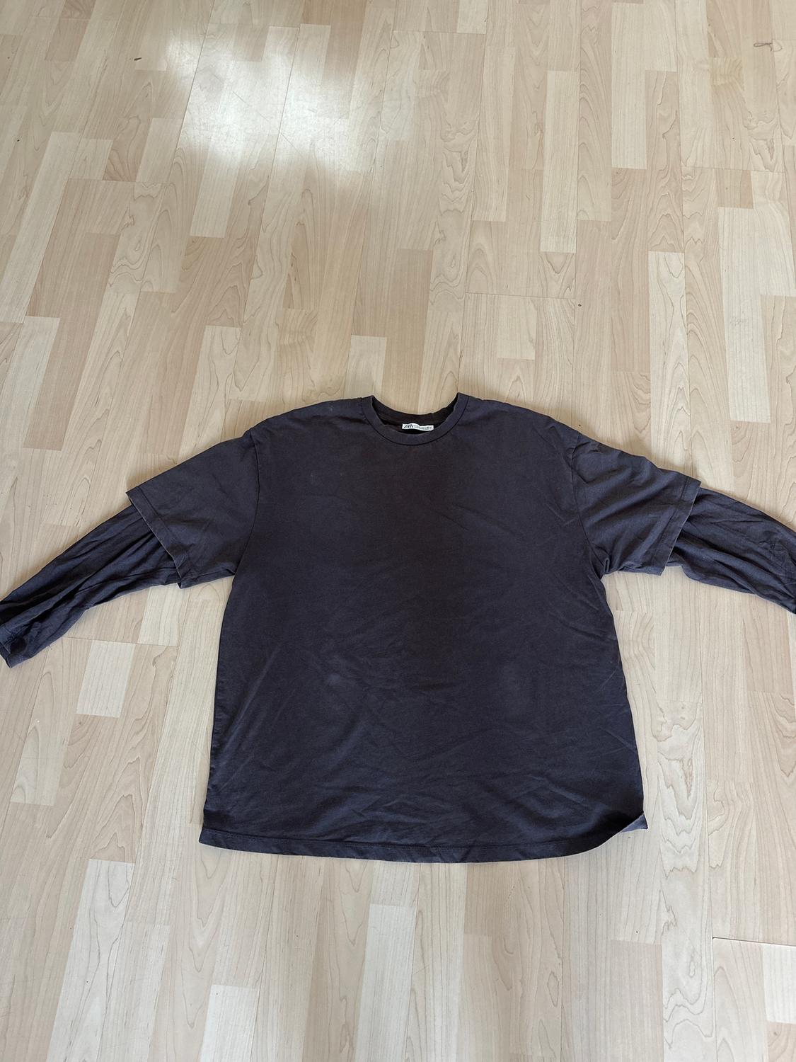 Black long-sleeved T-shirt laid out on a light wooden floor, showcasing its simple and casual design.