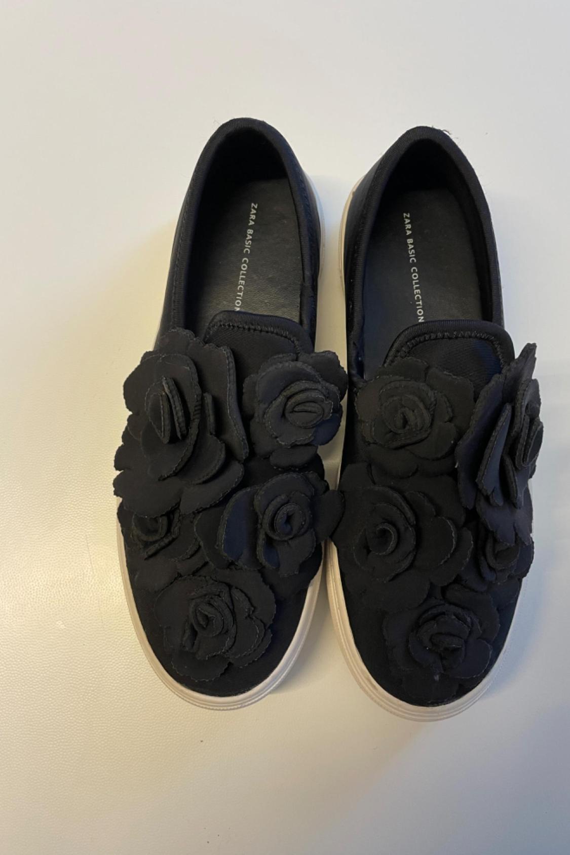 Front view of black trainers with floral applications on the upper.