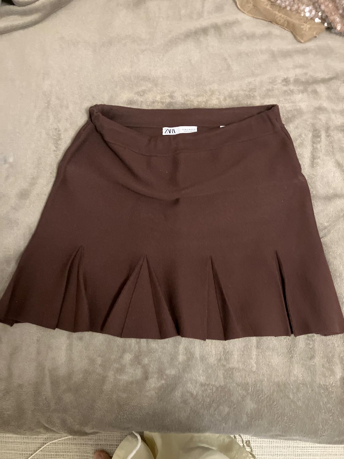 Short brown pleated skirt with a hemline detail and Zara label, laid out on a soft, light-coloured surface.