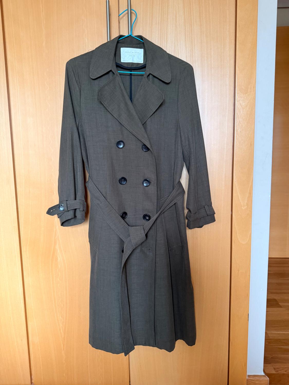 Double-breasted brown coat hanging on a blue hanger over a light wooden door.