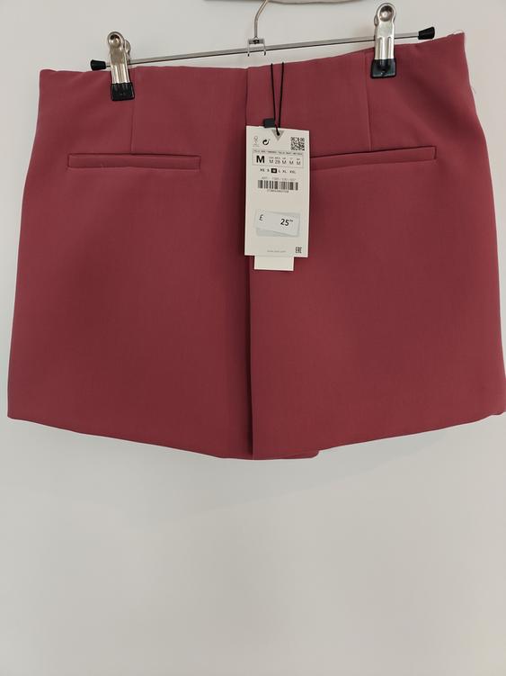 Dark red mini skirt hanging on a hanger with a £25 price tag. Decorative back pockets visible.