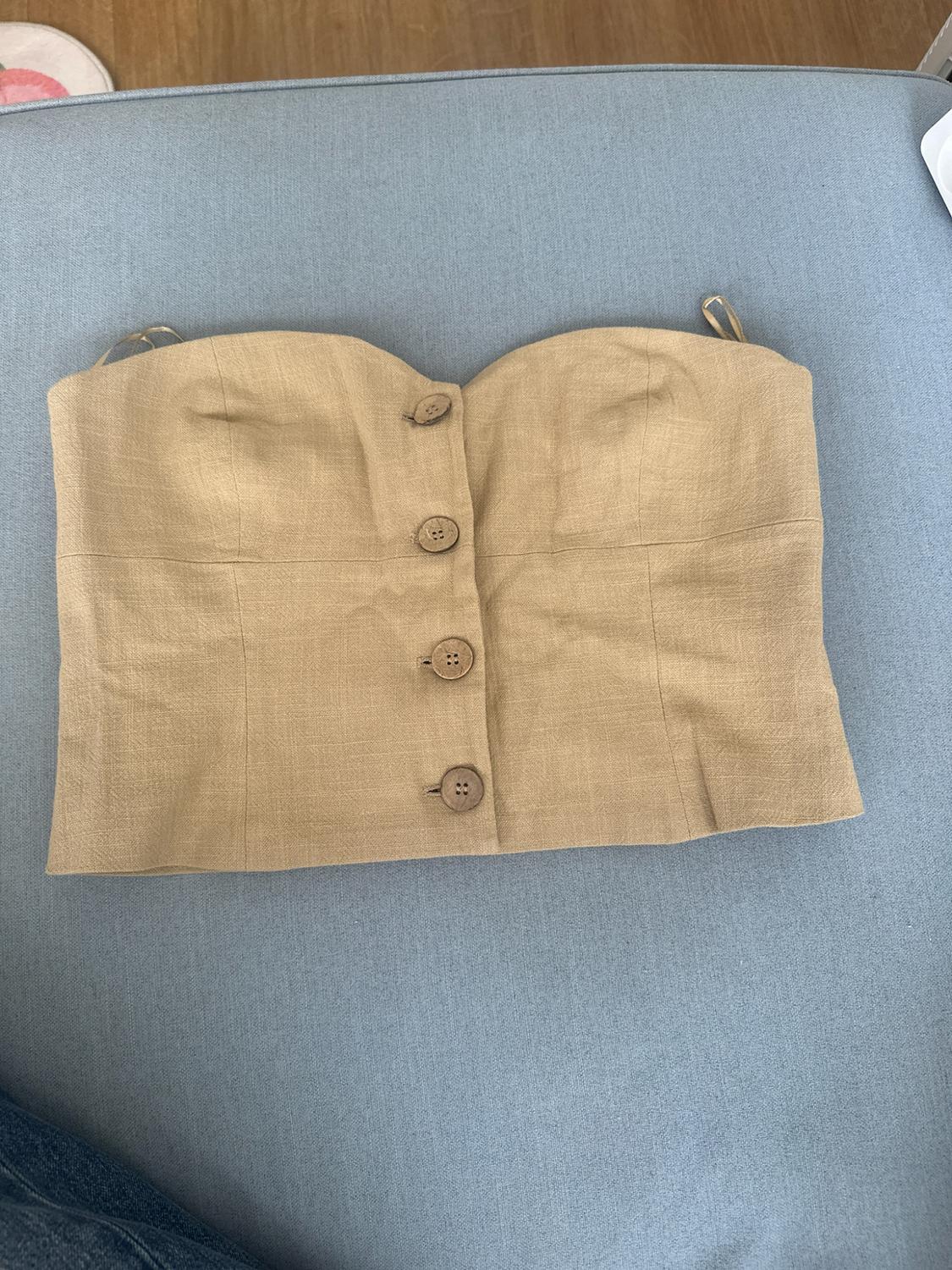 Beige strapless top with front buttons on a light blue surface. Casual, relaxed-style composition.
