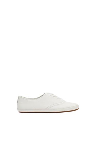 White profile trainer with laces, a textured finish and a thin brown sole, set against a minimalist white background.