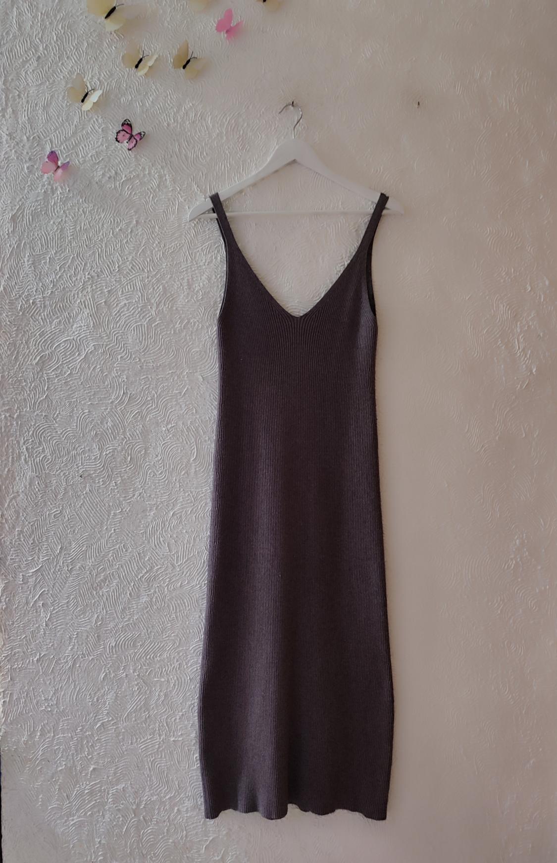 Dark grey strappy dress hanging on a white hanger against a textured wall with decorative butterflies.