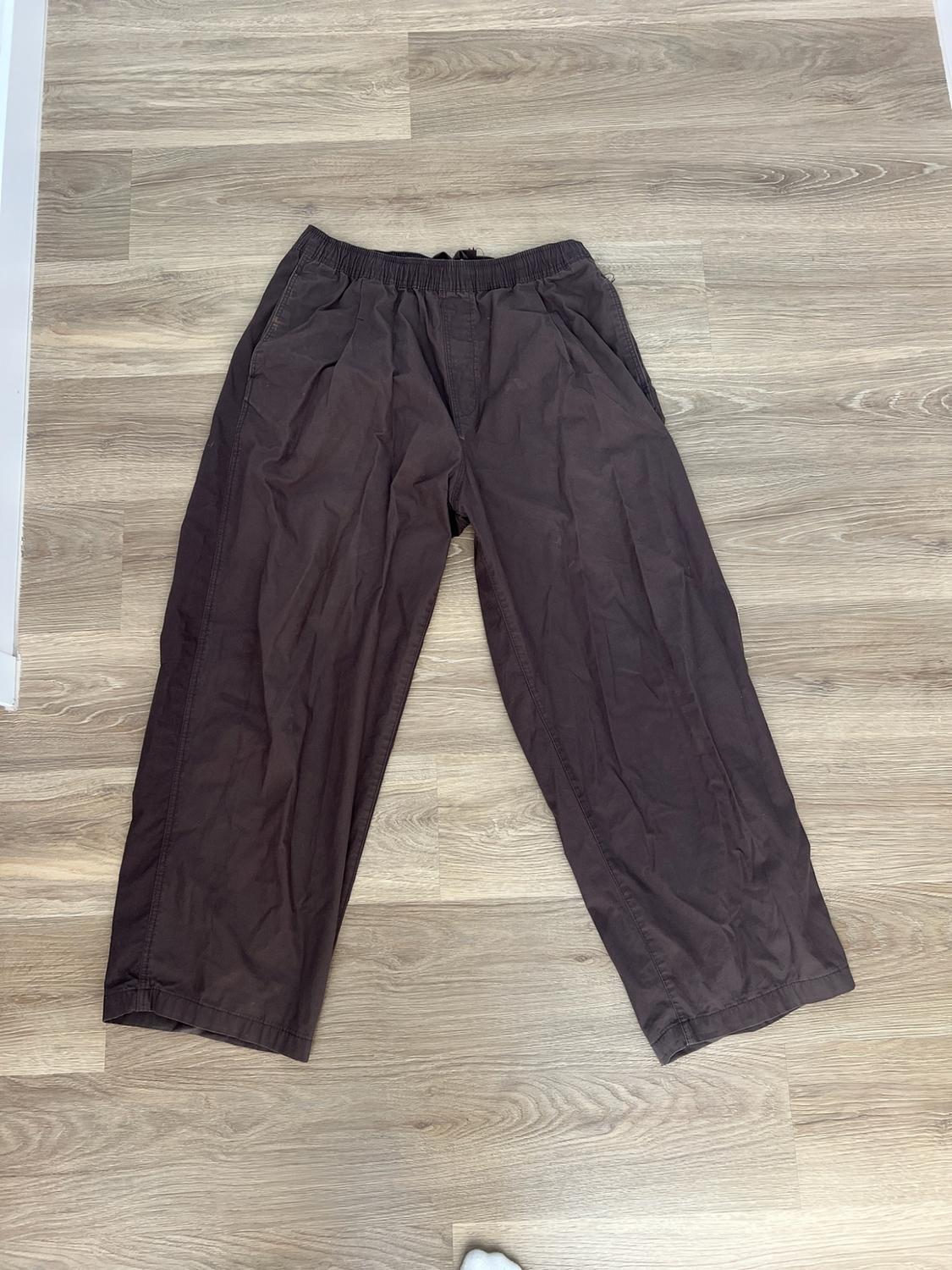 Dark brown wide-leg trousers with an elasticated waistband, laid out on a light wood floor. Casual and relaxed style.