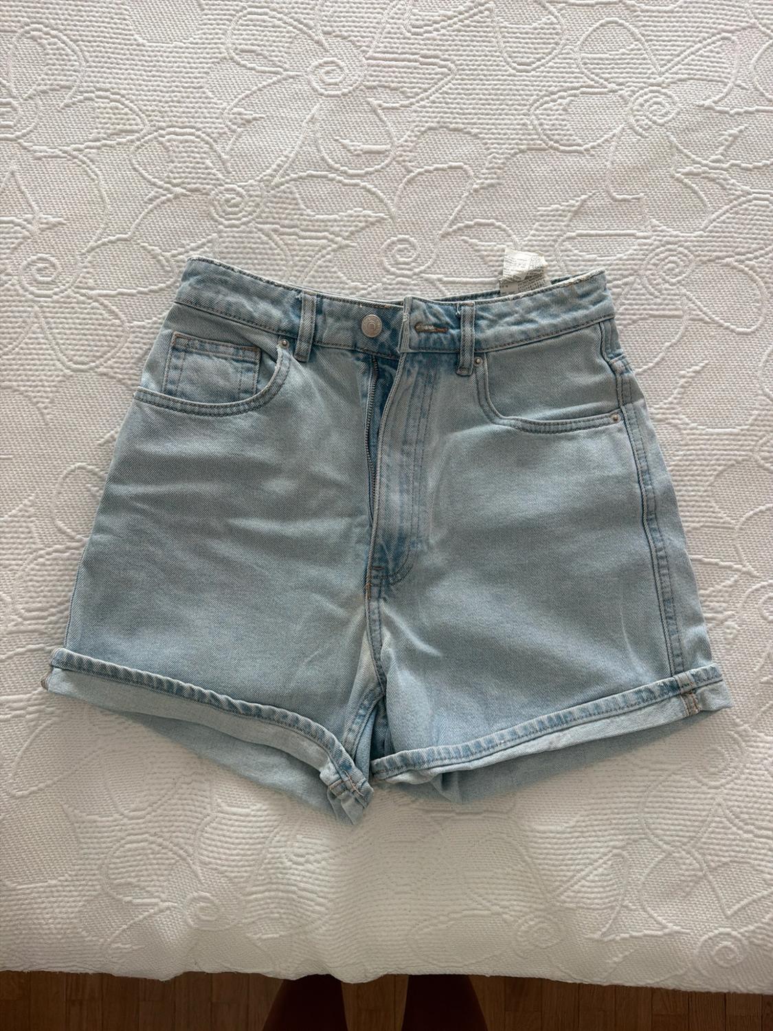 Light blue denim shorts with a hem, on a white bedspread with a floral texture. Relaxed and casual composition.