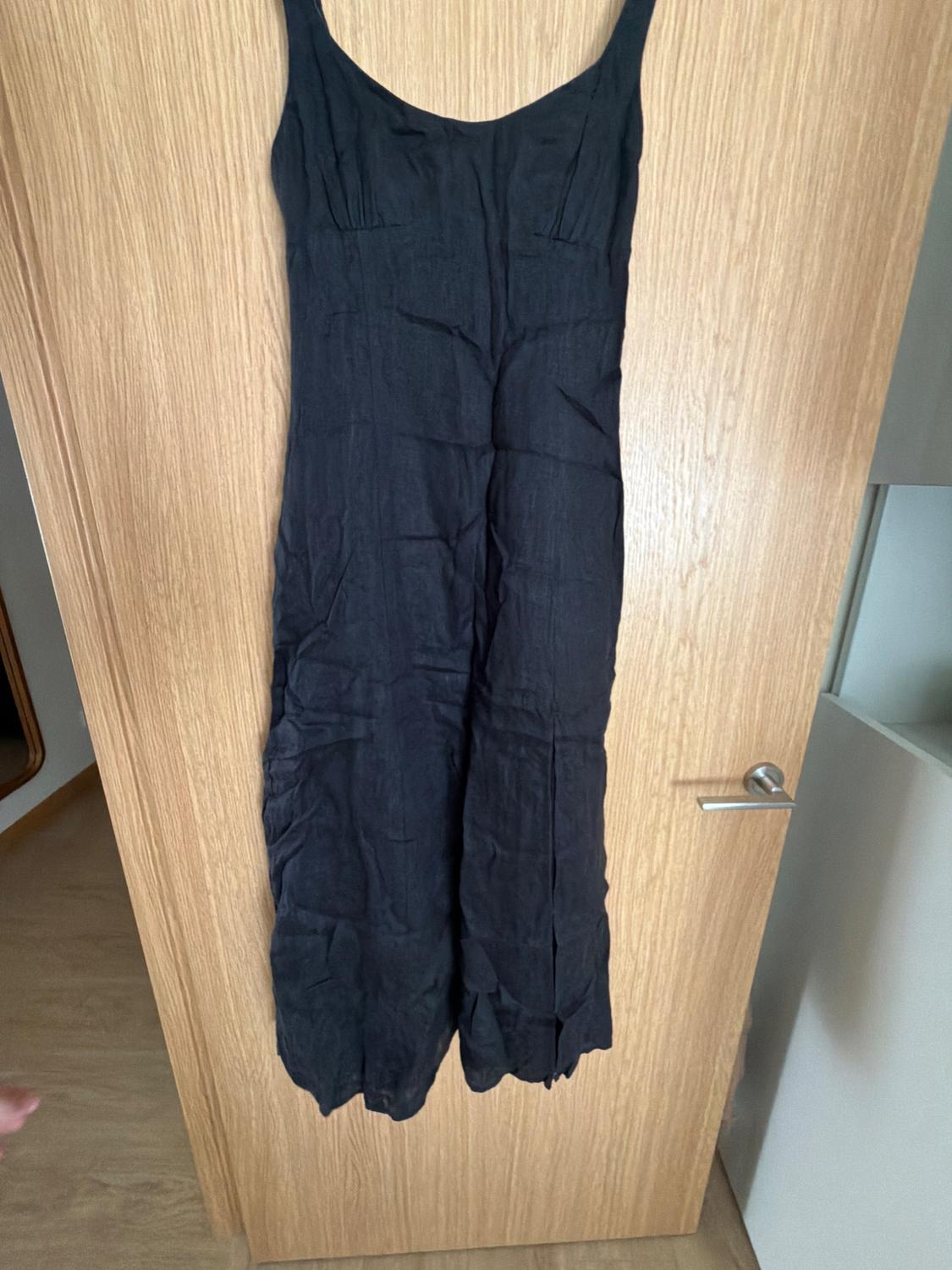 Black cami jumpsuit hanging on a light wooden door.