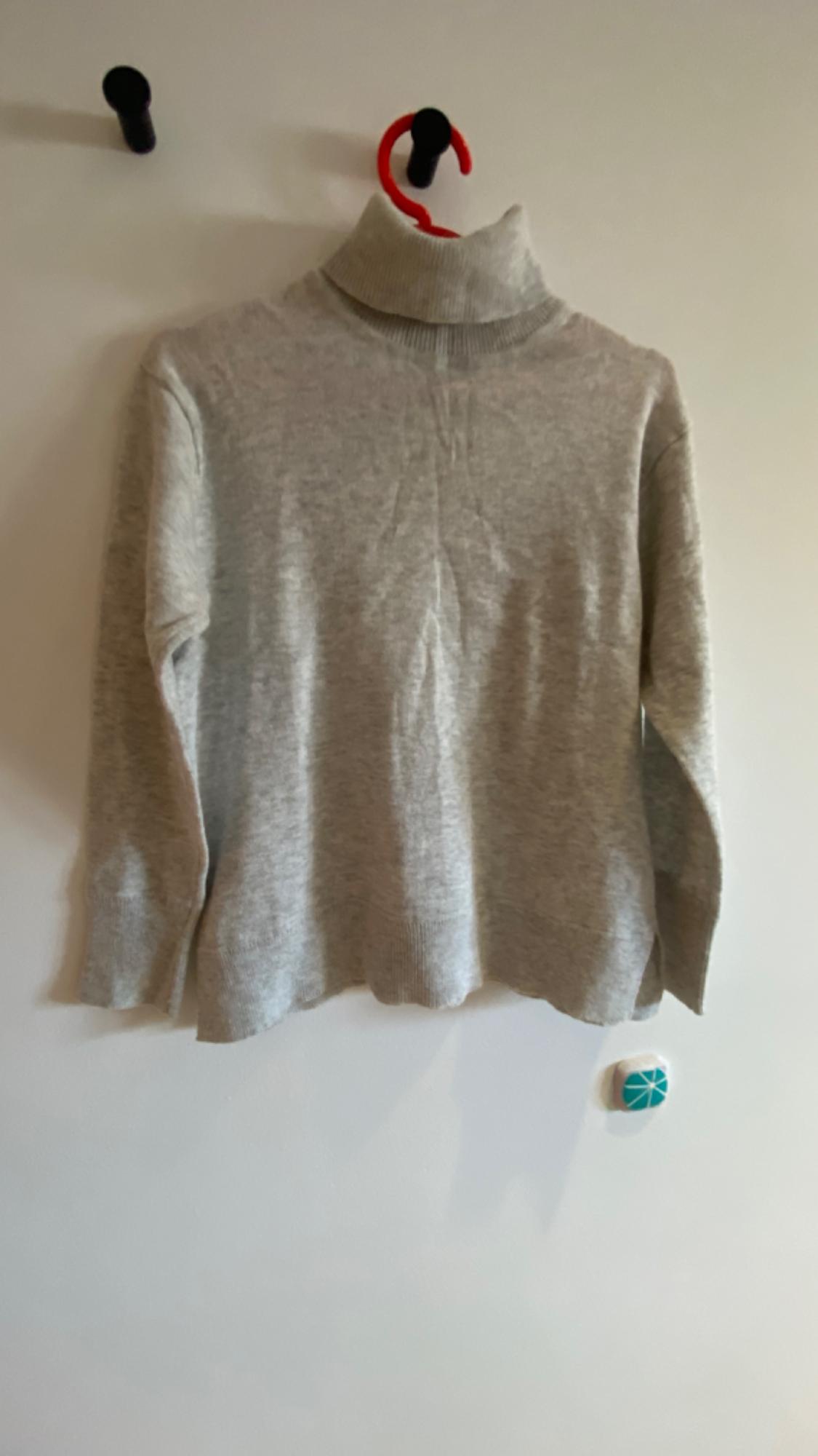 Grey roll-neck jumper hanging on a red hanger against a white wall.