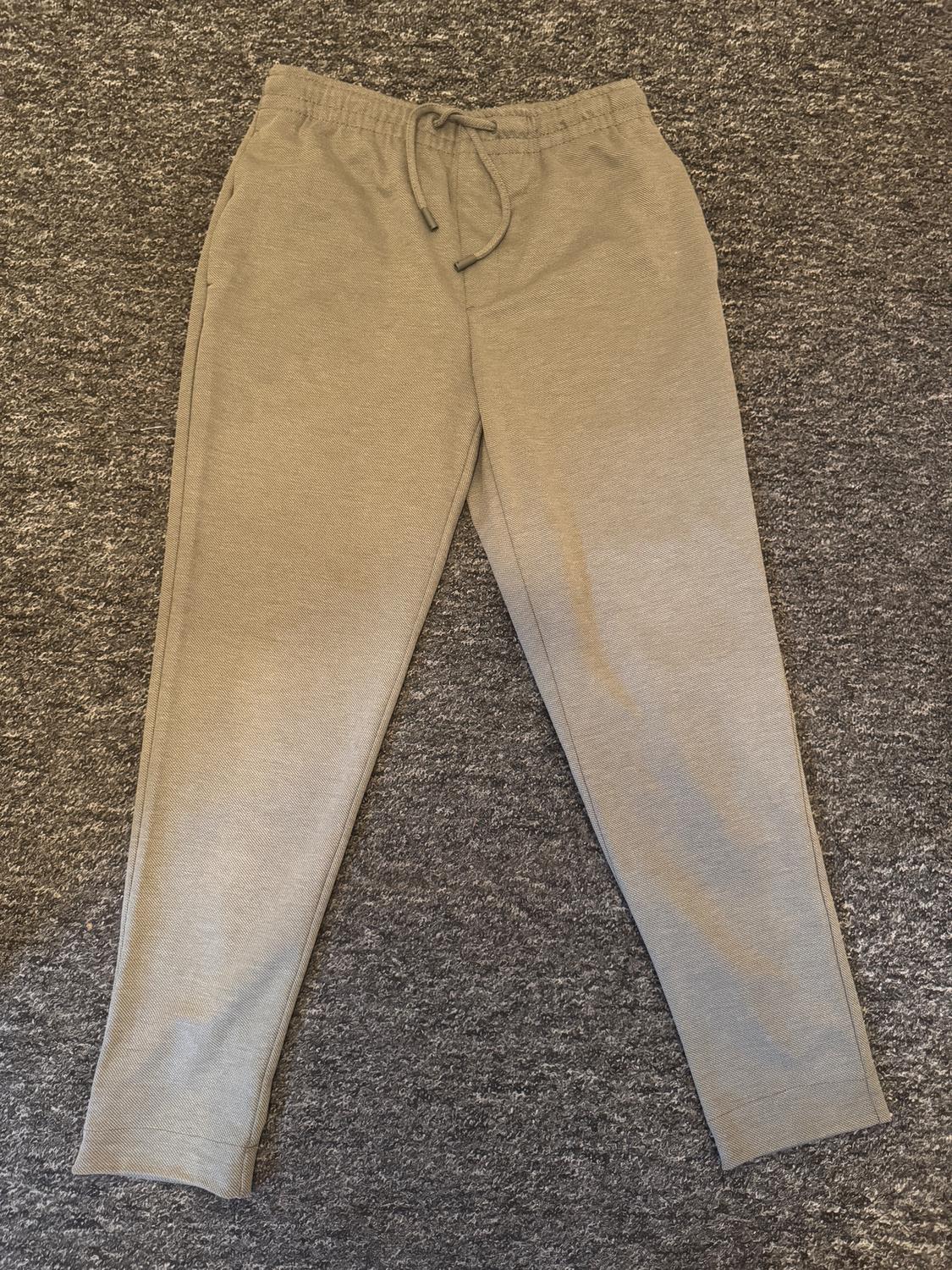 Grey jogging bottoms with an elasticated drawstring waist, laid on a grey rug.