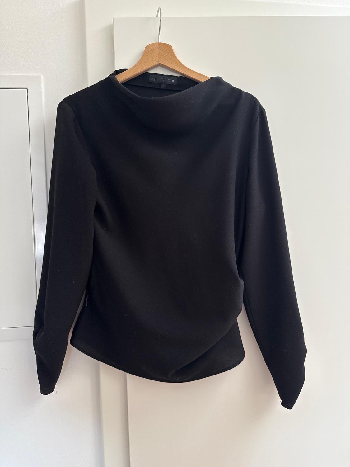 Black long-sleeved jumper hanging on a wooden hanger over a white door.