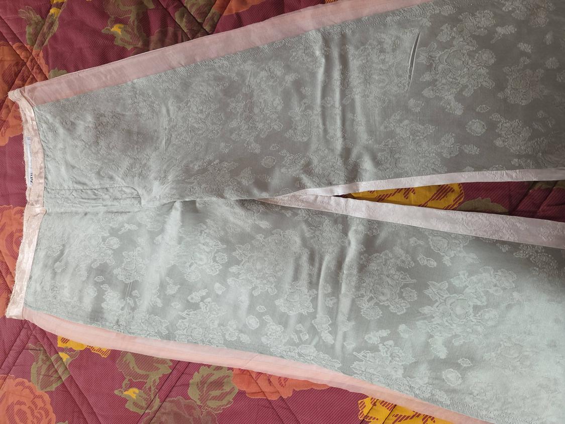 Grey fabric trousers with an embossed floral print, on a red and orange toned bedspread with a leaf design.