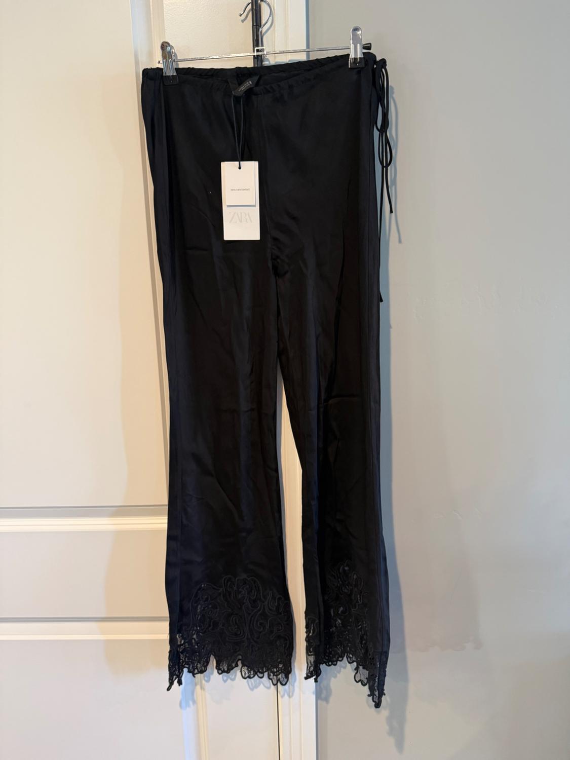 Black pants with a lace hem hanging on a hanger over a white door. Label with the text ZARA.