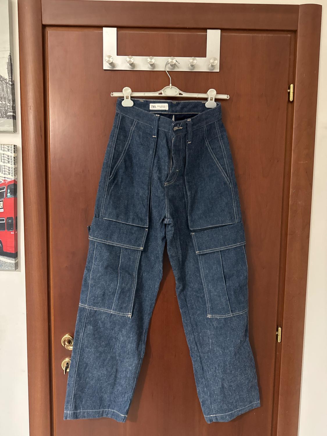 Blue denim cargo trousers hanging on a wooden door. To the left, an image of a red bus in London.