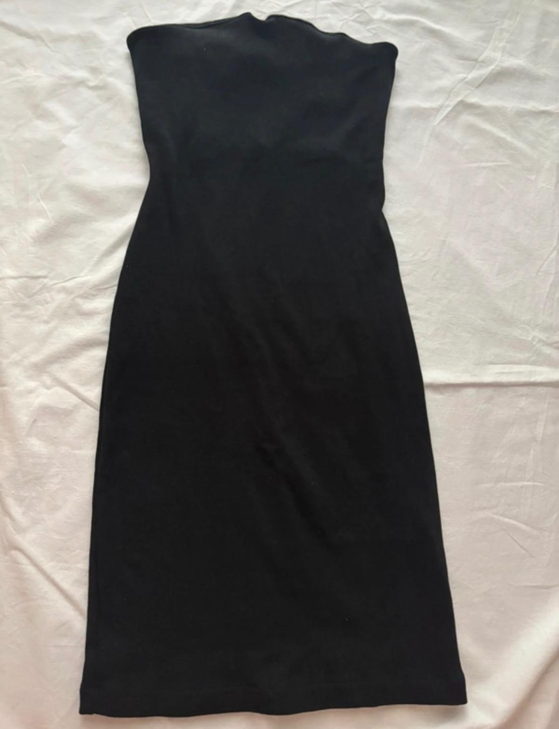 Plain black strapless, close-fitting dress laid out on crumpled white fabric.