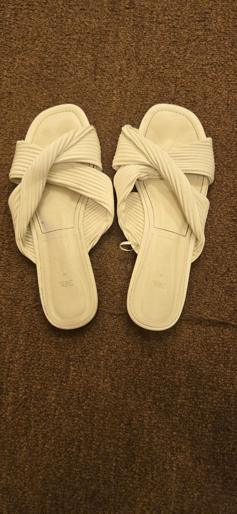 Front view of white sandals with crossover straps on a brown rug.