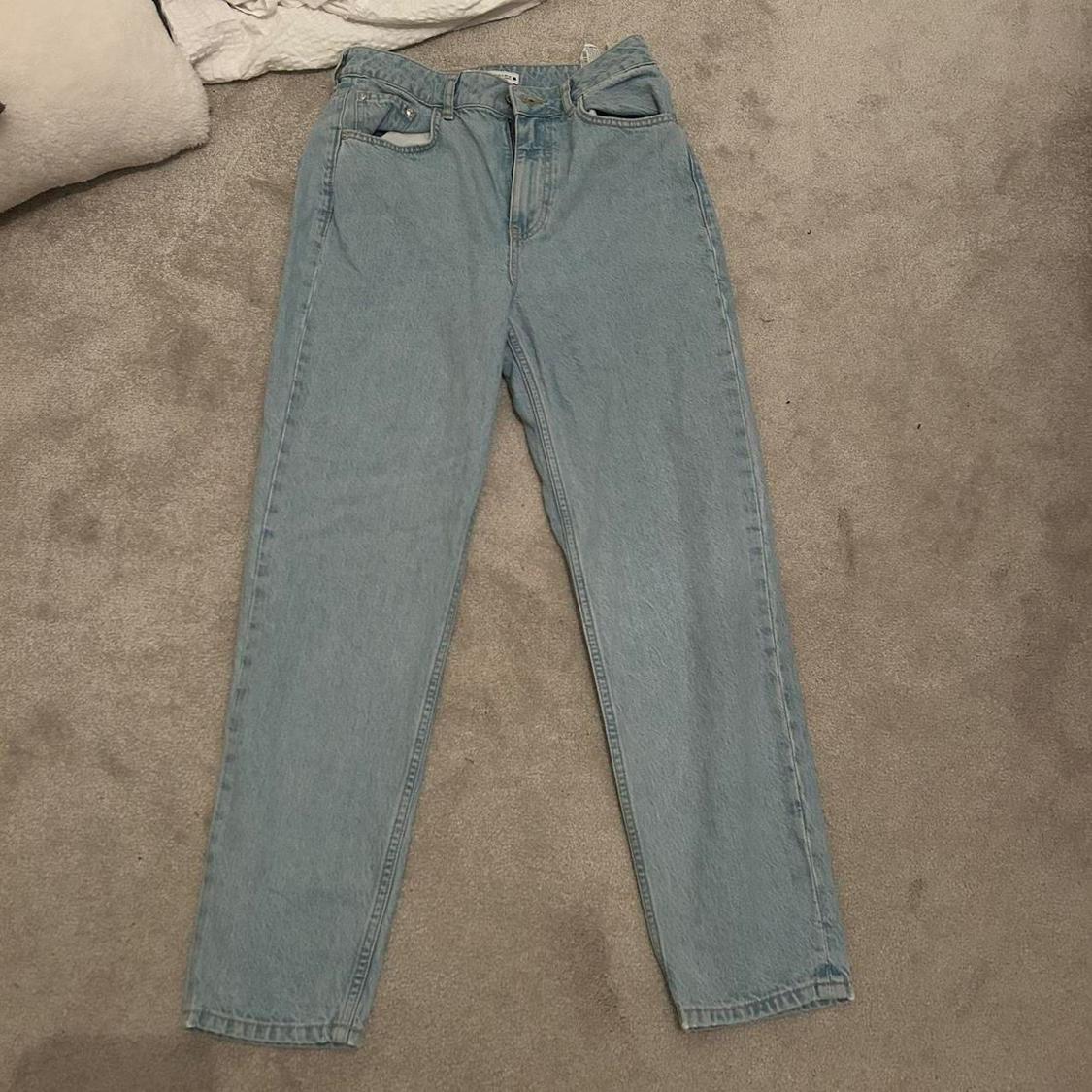 Light blue denim jeans placed on a beige rug, with a white blanket visible in the top left corner.