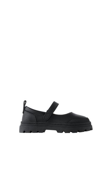 Black Mary Jane shoes with a chunky cleated sole, an instep strap and a back pull tab, on a white background.