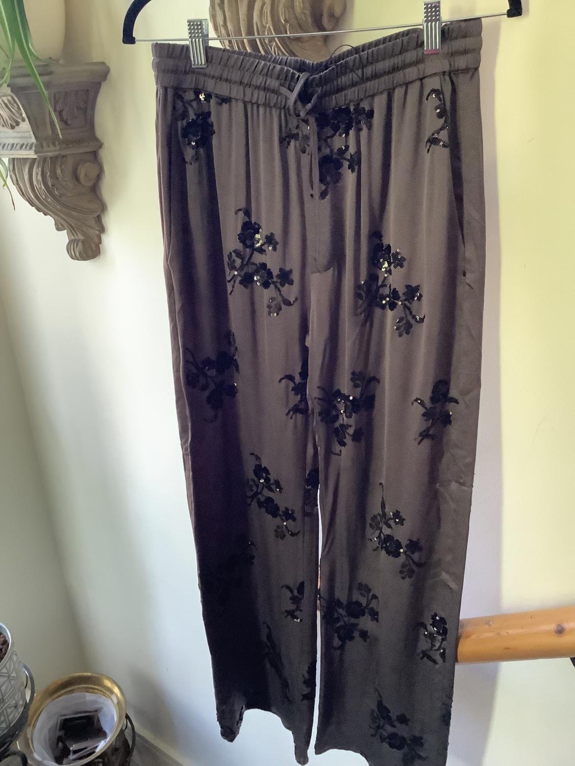 Brown trousers hanging on a hanger, with a black floral print and shiny details, in a well-lit indoor setting.
