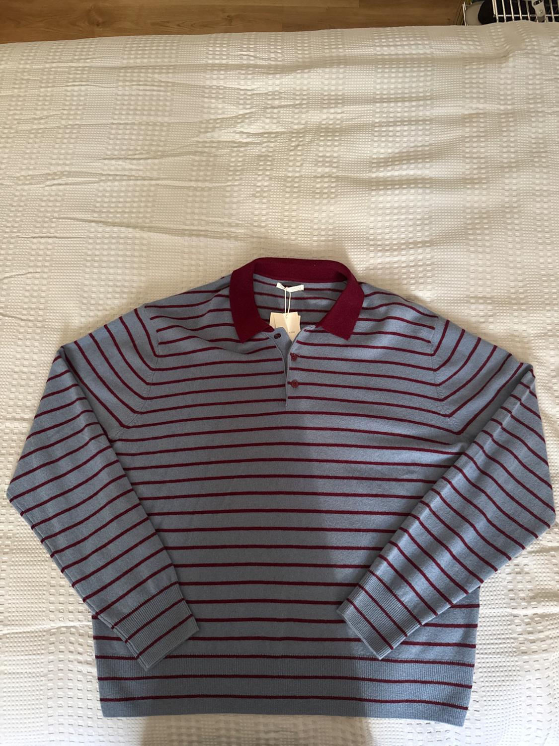 Blue long-sleeved polo shirt with horizontal stripes and a maroon collar, on a textured white bedspread in a relaxed setting.