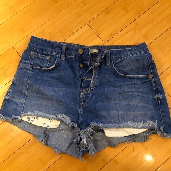 Blue denim shorts with buttons and a frayed hem on a wooden floor. The lining reads PRETTY WHEN YOU ARE ALONE.