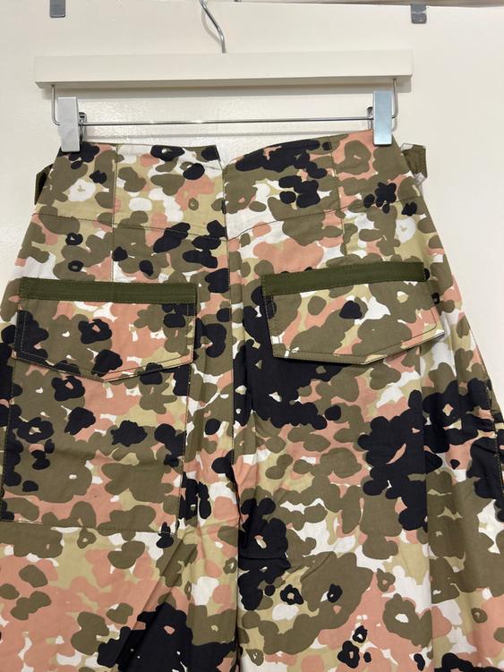 Hanging trousers with a camouflage print in green, pink, and black tones, with large back pockets and flaps.