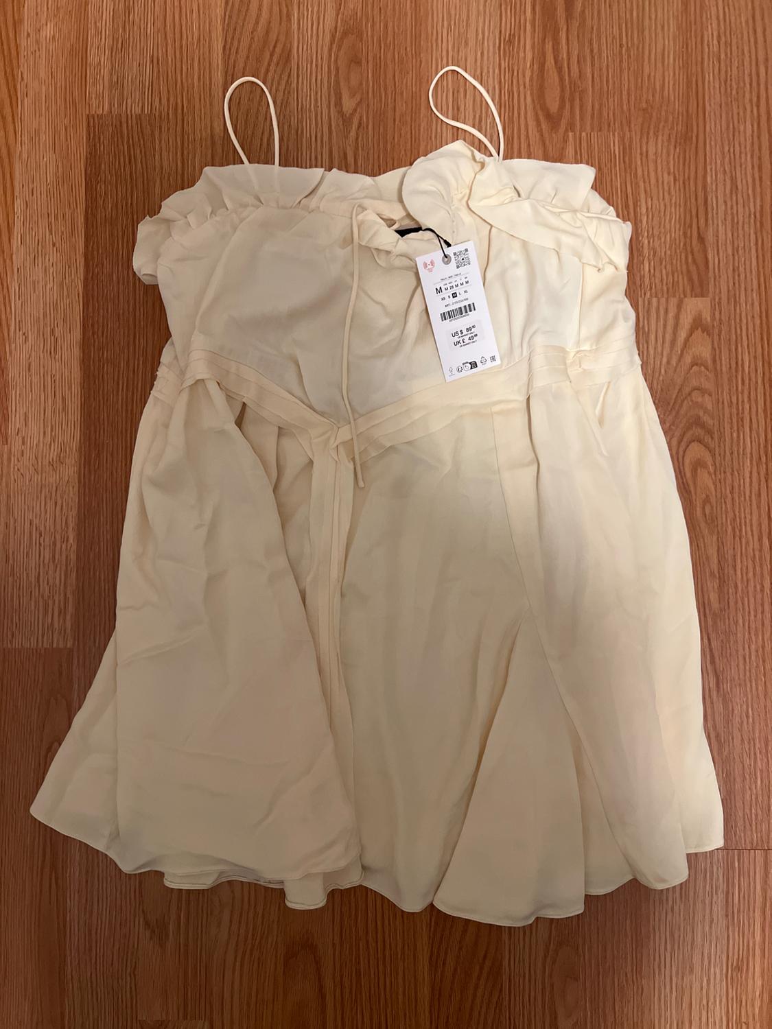 Beige dress with thin straps on a wooden floor. Visible label with size details and barcode.