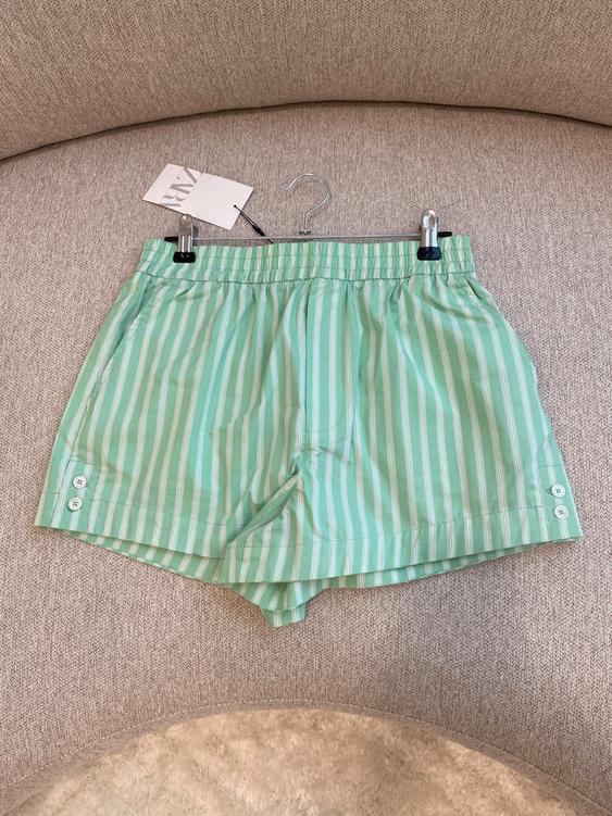 Green shorts with white stripes hanging on a hook above a beige sofa. Visible tag with text "ZARA".