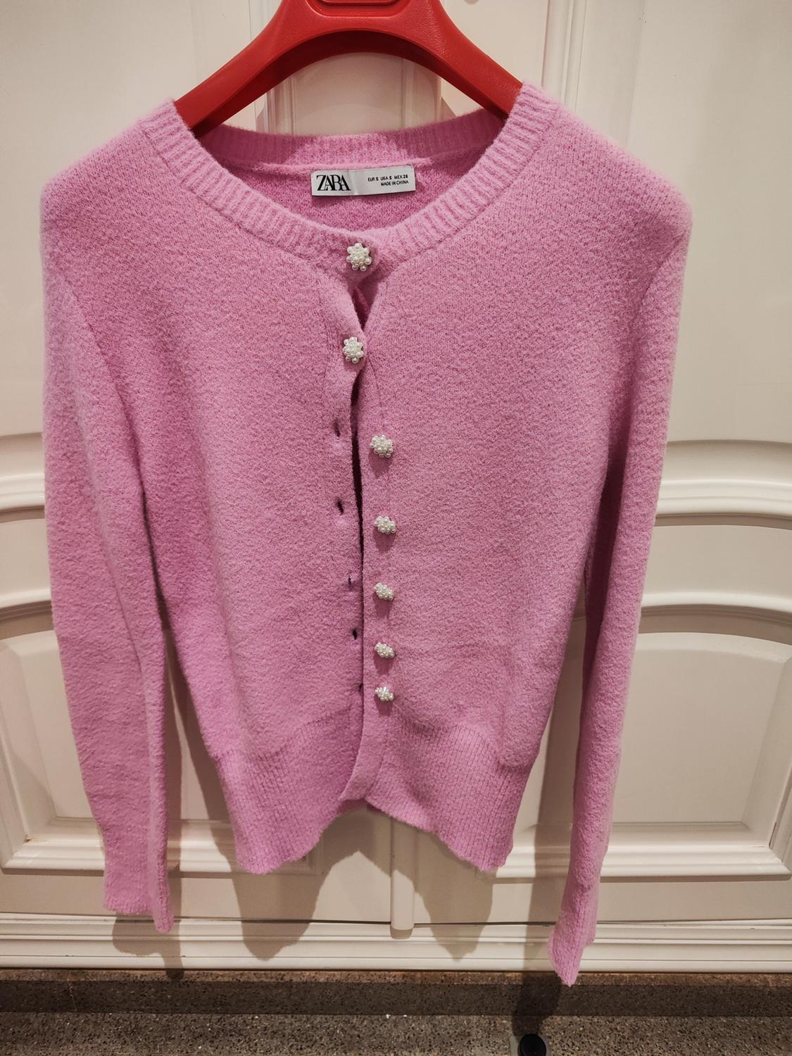 Front view of a pink cardigan with decorative flower-shaped buttons.