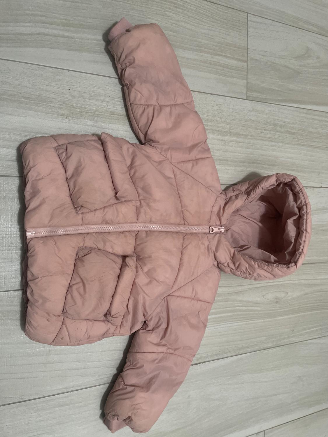 Pink padded jacket for a boy with a hood, front zip and pockets, on a light wooden floor.