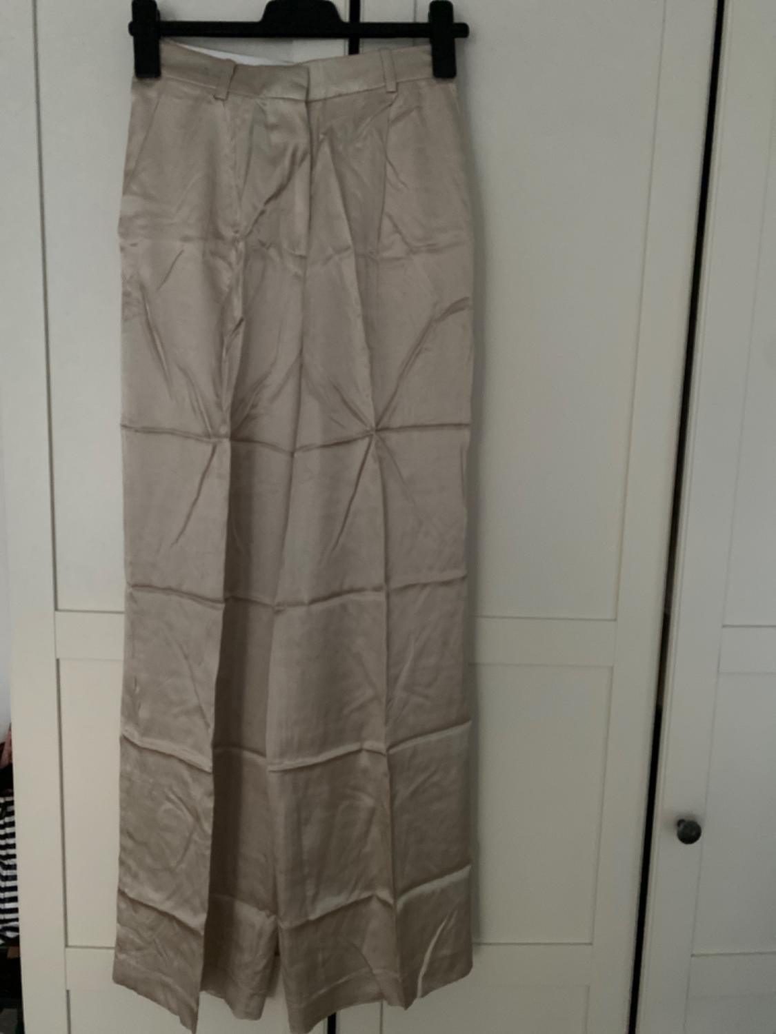Front view of beige trousers with pleats and side pockets.
