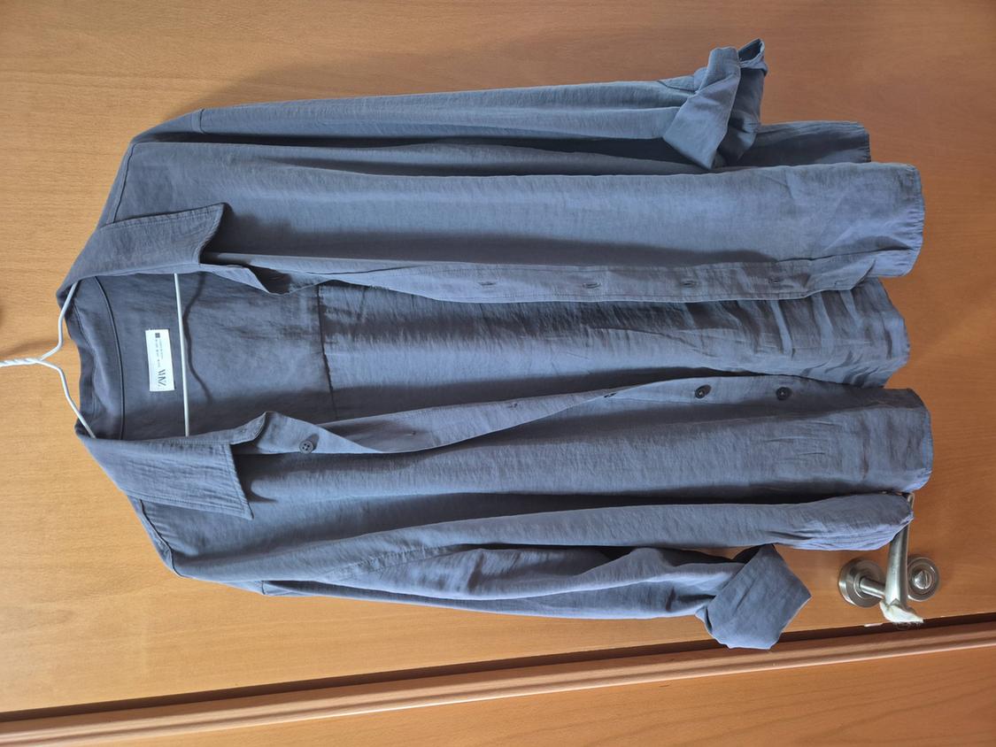 Grey long-sleeved shirt hanging on a white hanger over a wooden door. Visible tag with text "VIX".